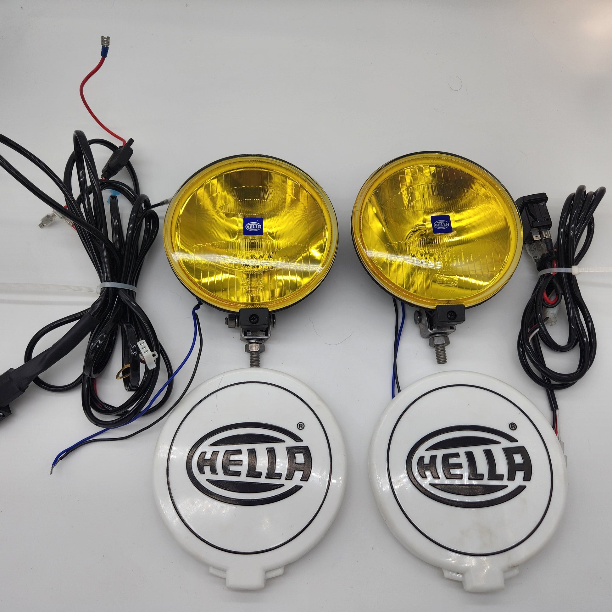 Two yellow Hella fog lights with wiring on a white background